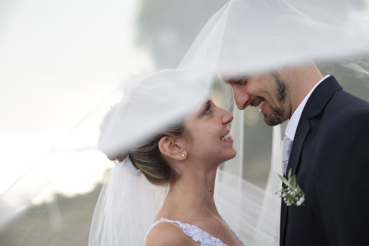 Smiling couple under wedding veil sharing a joyful moment. Perfect for romance themes.